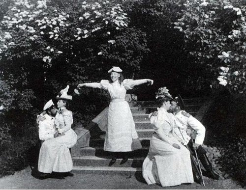 kootyl:

Tsar Nicholas II kissing Alexandra Romanov on the stairs in the garden of Peterhof while Nicholas’s sister Xenia sits in the lap of her husband Sandro and his younger sister Olga, seem to prepare to take flight.
