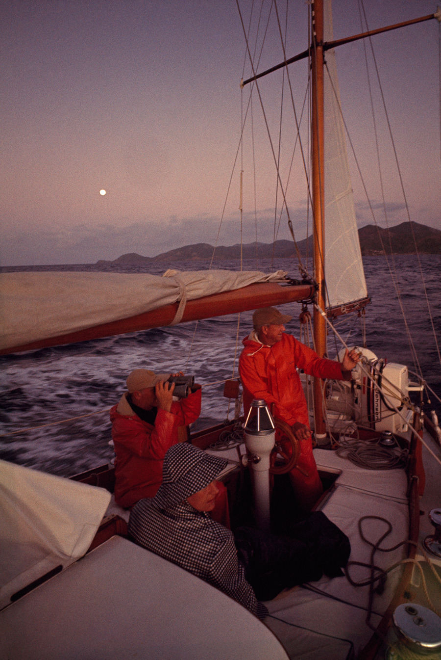 Sailors wearing raingear sit in a sailboat’s cockpit awaiting dawn in the West Indies, October 1966.Photograph by Winfield Parks, National Geographic