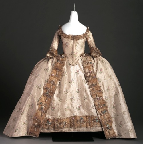  Court Gown, c. 1760 Silver tissue woven with multi-colored foil flowers and trimmed with gold lace European “The art of French dress had become so luxurious that by the eighteenth-century all of the European courts adopted French styles—even the staunchest enemies of France. In 1756 an English commentator noted, “The French designers are at present esteemed the most happy in their inventions. The natural freeness of composition is really admirable, and suited to the purpose intended for without crowding things together, but display them with a careless air, beauty and delicacy, and no wonder that all the rest of the European nations take the French fashion of ornaments, for their rule and pattern to imitate.” (via: Arizona Costume Institute)