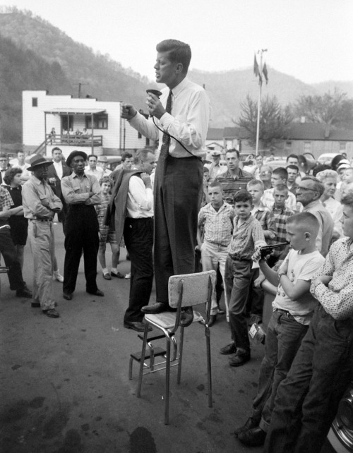 While part of every candidate’s retinue, security was simply not the pressing, public concern in 1960 that it would suddenly and necessarily become within a few short years. Here, seemingly alone in a crowd in Logan County, West Virginia, JFK speechifies from a kitchen chair as, mere feet away, a young boy absently plays with a jarringly realistic-looking toy gun.
