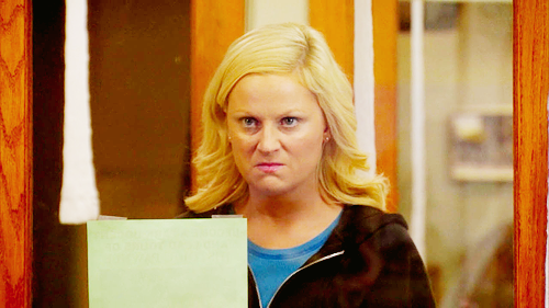 Leslie Knope from Parks & Recreation wearing a blue shirt and a black hoodie, scowling