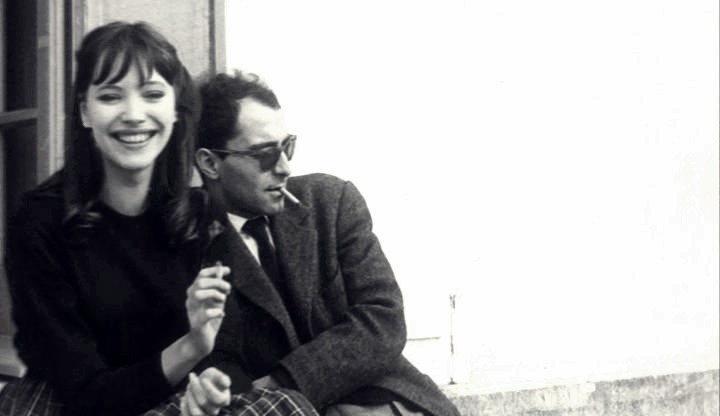 THIS IS THE STORY OF HOW ANNA KARINA & JEAN-LUC GODARD FIRST “GOT TOGETHER”
Anna Karina: That happened while we were shooting the picture in Geneva. It was a strange love story from the beginning. I could see Jean-Luc was looking at me all the time, and I was looking at him too, all day long.  We were like animals. One night we were at this dinner in Lausanne. My boyfriend, who was a painter, was there too. And suddenly I felt something under the table – it was Jean-Luc’s hand. He gave me a piece of paper and then left to drive back to Geneva. I went into another room to see what he’d written.  It said, “I love you.  Rendezvous at midnight at the Café de la Prez.” And then my boyfriend came into the room and demanded to see the piece of paper, and he took my arm and grabbed it and read it.  He said, “You’re not going.” And I said, “I am.” And he said, “But you can’t do this to me.”  I said, “But I’m in love too, so I’m going.” But he still didn’t believe me. We drove back to Geneva and I started to pack my tiny suitcase.  He said, “Tell me you’re not going.” And I said, “I’ve been in love with him since I saw him the second time. And I can’t do anything about it.” It was like something electric. I walked there, and I remember my painter was running after me crying. I was, like, hypnotized – it never happened again to me in my life.
So I get to the Cafe de la Prez, and Jean-Luc was sitting there reading a paper, but I don’t think he was really reading it. I just stood there in front of him for what seemed like an hour but I guess was not more than thirty seconds. Suddenly he stopped reading and said,” Here you are. Shall we go?” So we went to his hotel. The next morning when I woke up he wasn’t there. I got very worried. I took a shower, and then he came back about an hour later with the dress I wore in the film - the white dress with flowers. And it was my size, perfect. It was like my wedding dress.
We carried on shooting the film, and, of course, my painter left. When the picture was finished, I went back to Paris with Jean-Luc, Michel Subor, who was the main actor, and Laszlo Szabo, who was also in the film, in Jean-Luc’s American car. We were all wearing dark glasses and we got stopped at the border – I guess they thought we were gangsters. When we arrived in Paris, Jean-Luc dropped the other two off and said to me, “Where are you going?”  I said, “I have to stay with you. You’re the only person I have in the world now.” And he said, “Oh my God.”
Extract taken from an interview with Anna Karina conducted by Graham Fuller in Projections 13: Women Film-makers on Film-making, edited by Isabella Weibrecht, John Boorman and Walter Donohue (Faber & Faber, 2004) 
(via Focus Features)