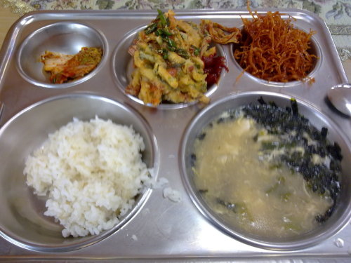 Clockwise from top left: kimchi; fried tangles of crab sticks and scallions with soy sauce and gochujang; shredded dry mollusk in spicy-sweet sauce; ddeokguk without ddeok, with large quantity of dry seaweed shreds in the top-right of the bowl; rice.